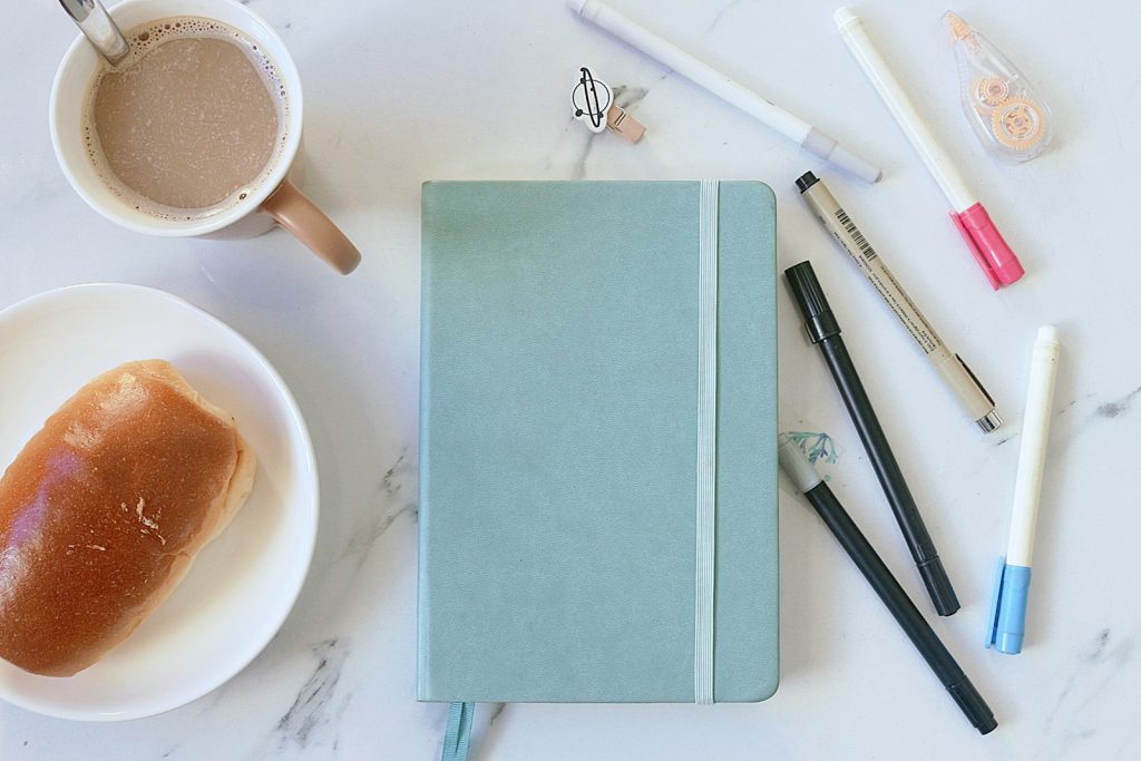 Light blue notebook, coffee and pens on marble
