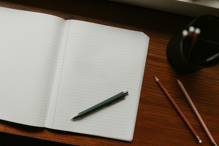 Open notebook with a pen and pencils on a desk