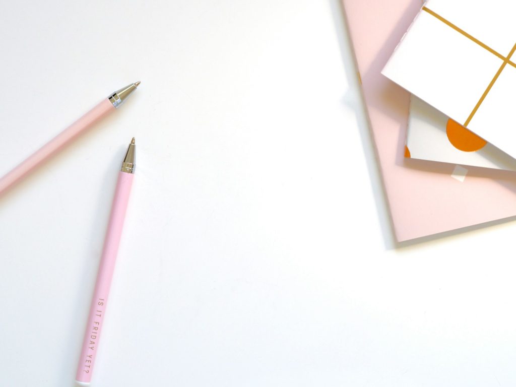 Two pink pens beside a notebook