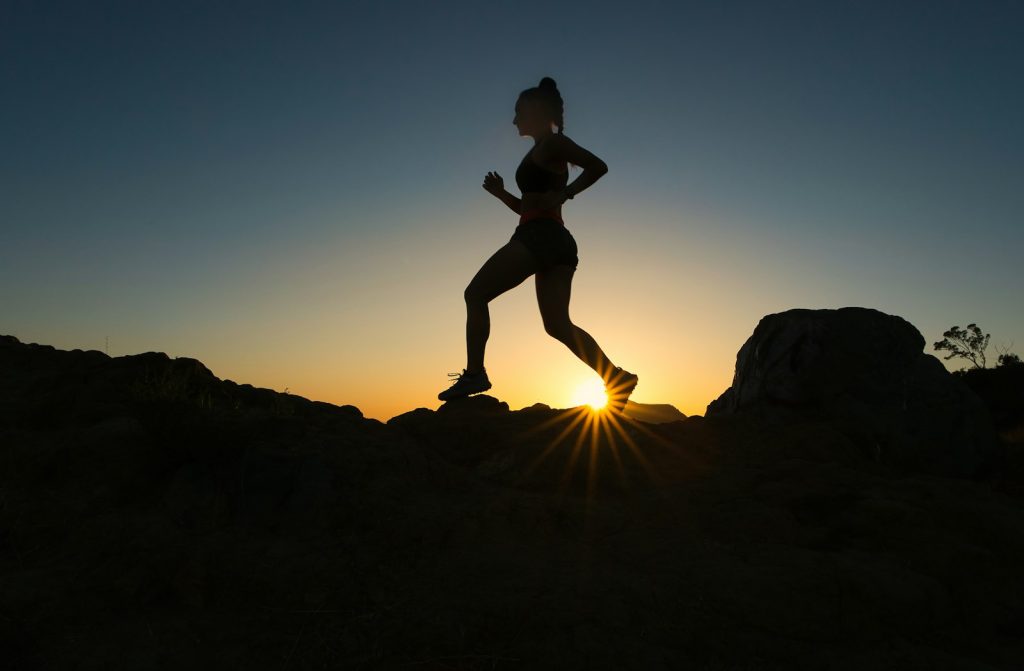 Runner in silhouette on a rocky trail at sunset