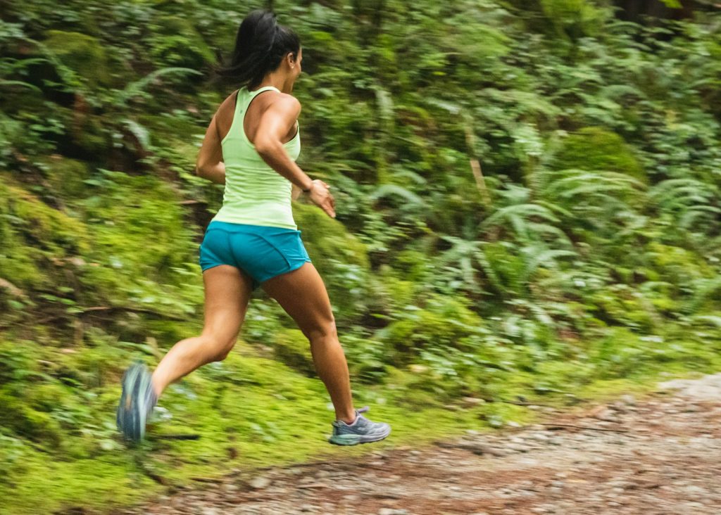 Woman in white tank top running on a forest dirt road