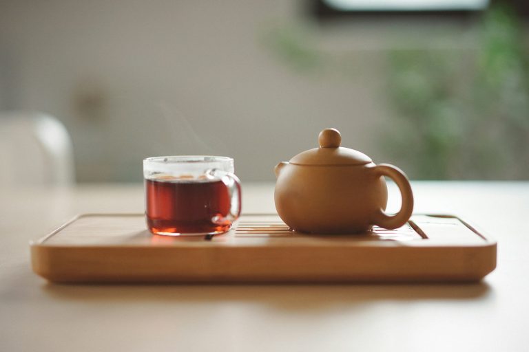 Glass cup of tea beside a ceramic teapot